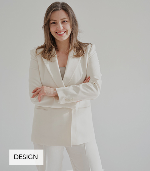 Tanja Grill, Gründerin und Creative Director bei TANOLARA im eleganten cremefarbenen Hosenanzug steht vor hellem Hintergrund, verschränkt die Arme und lächelt selbstbewusst in die Kamera.