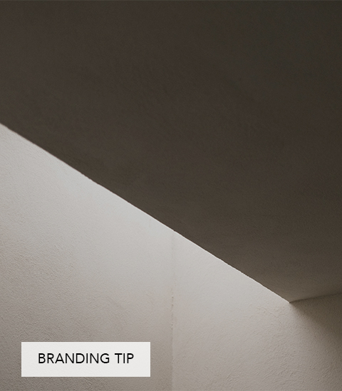 Minimalistische Architekturaufnahme mit Licht und Schatten: Ein schmaler Lichtstreifen fällt zwischen Wand und Decke und erzeugt eine klare geometrische Komposition. Unten links steht der Text „Branding Tip“.