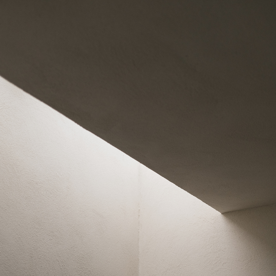 Überschrift "Logo vs. Marke" auf minimalistischer Architekturaufnahme mit Licht und Schatten – ein schlichter, geometrischer Ausschnitt einer weißen Wand, der Ruhe und Klarheit ausstrahlt.