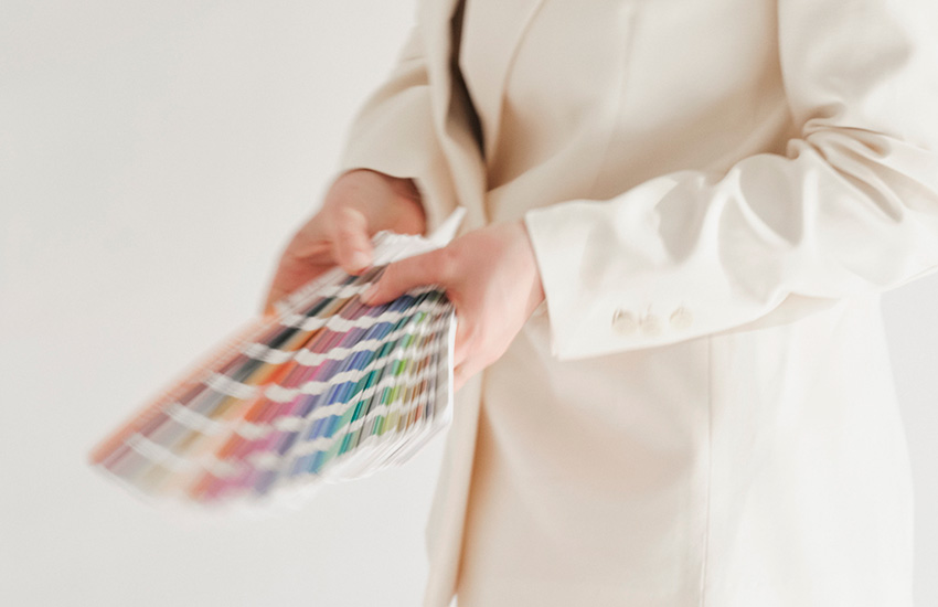 TANOLARA Branding Process; Eine Person im cremefarbenen Blazer hält einen aufgefächerten Farbfächer mit zahlreichen bunten Farbmustern in den Händen.