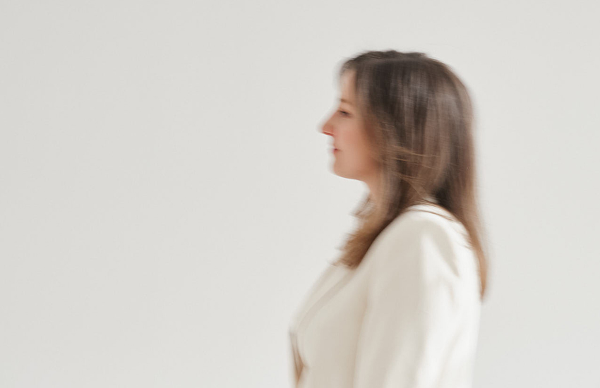 Unscharfes Porträt einer Frau im weißen Blazer, seitlich aufgenommen, vor hellem Hintergrund in minimalistischer Ästhetik.