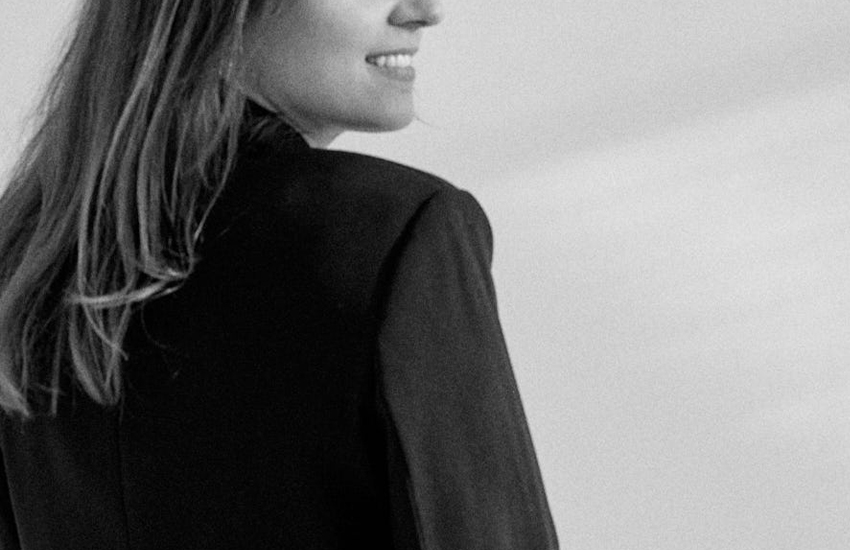 Schwarz-weiß Fotografie einer Frau im schwarzen Blazer, die seitlich in die Kamera lächelt und eine positive, elegante Ausstrahlung vermittelt.